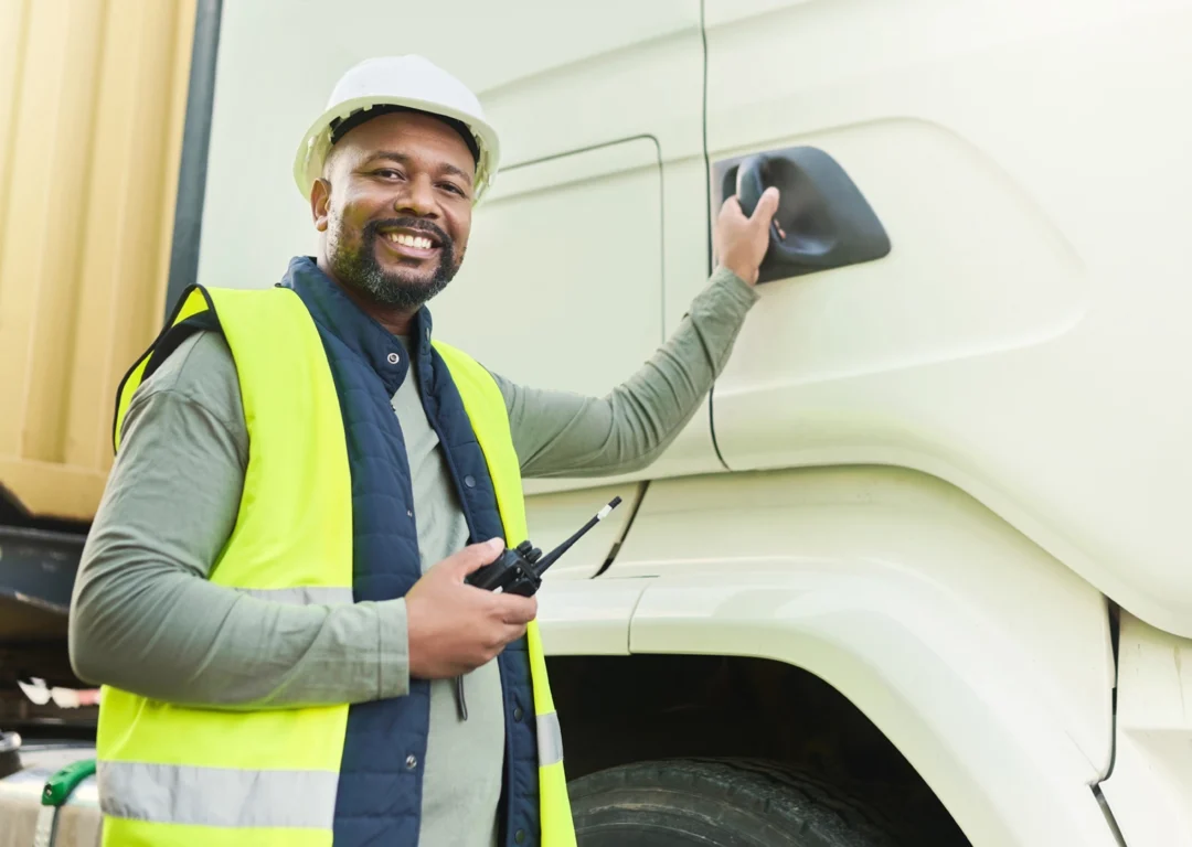 Male driver in hard hat and hi-vis standing next to an HGV.