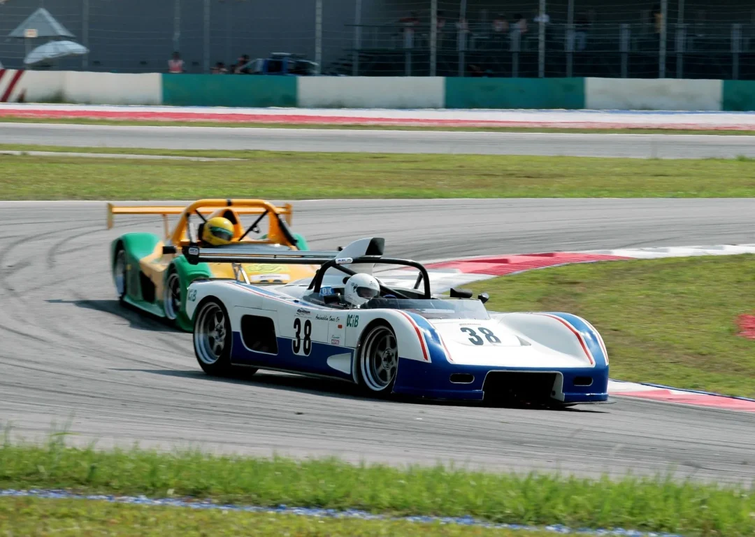 One white and one yellow open-top race cars on a racetrack.
