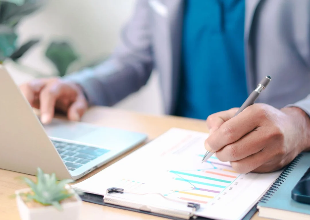 A doctor working at a desk with a notepad and laptop.