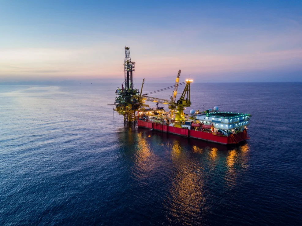 An offshore oil rig and support vessel illuminated at dusk, representing the high-risk environments that require safety-critical medical certifications.